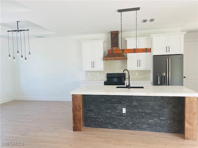 kitchen with visible vents, wall chimney range hood, a large island, stainless steel fridge, and a sink