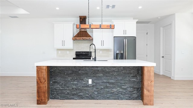 kitchen featuring visible vents, an island with sink, a sink, black range with electric cooktop, and stainless steel refrigerator with ice dispenser