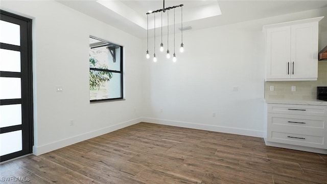 unfurnished dining area featuring baseboards, a raised ceiling, dark wood-type flooring, and visible vents