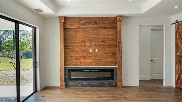 unfurnished living room with a barn door, wood finished floors, baseboards, and a glass covered fireplace