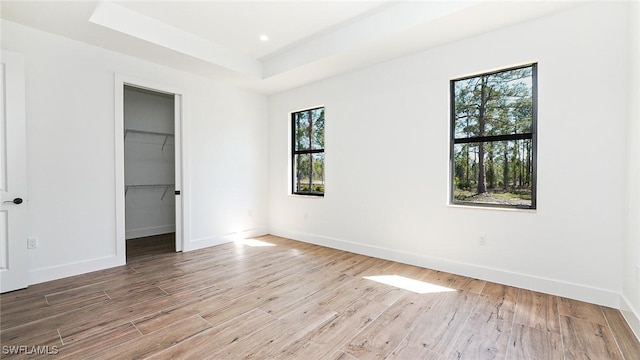 unfurnished bedroom featuring a tray ceiling, baseboards, wood finished floors, and a spacious closet