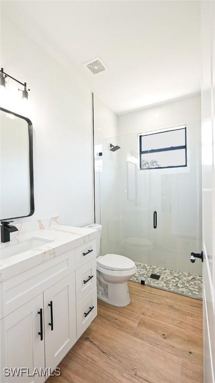 bathroom featuring visible vents, toilet, a stall shower, wood finished floors, and vanity