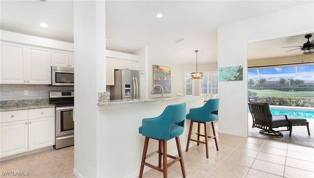 kitchen with decorative backsplash, appliances with stainless steel finishes, white cabinetry, light stone countertops, and a kitchen bar