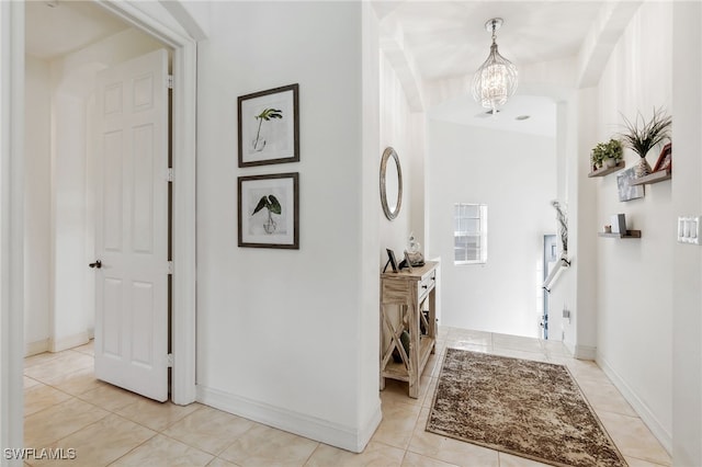 corridor featuring light tile patterned flooring, baseboards, and a chandelier