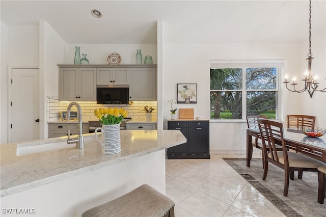 kitchen featuring light stone countertops, an inviting chandelier, a sink, hanging light fixtures, and tasteful backsplash