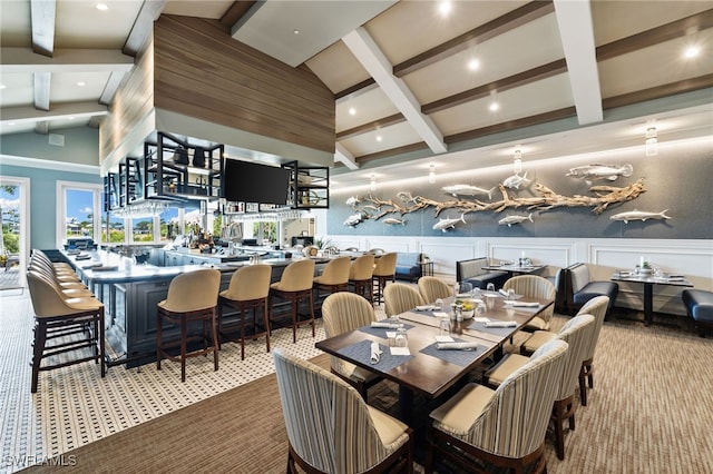 carpeted dining area featuring a decorative wall, vaulted ceiling with beams, and a wainscoted wall