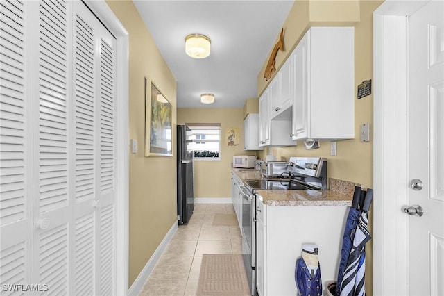 kitchen with white microwave, light tile patterned floors, stainless steel range with electric cooktop, freestanding refrigerator, and white cabinetry