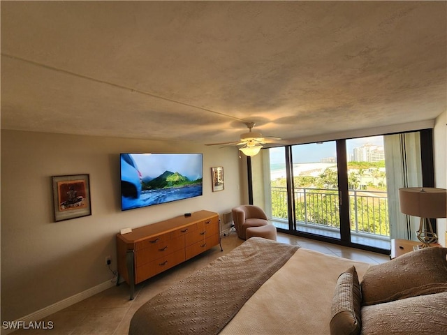 living room featuring light tile patterned floors, baseboards, a wall of windows, and a ceiling fan