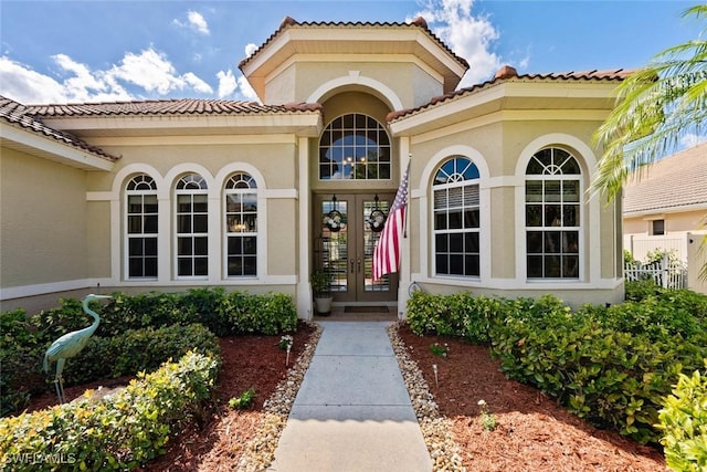 view of exterior entry with stucco siding, fence, and french doors