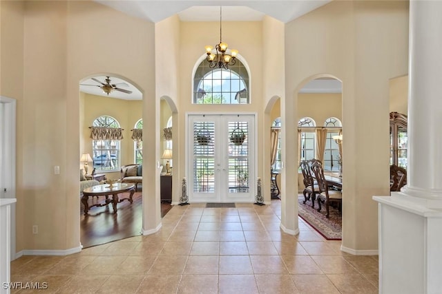 entrance foyer with french doors, a high ceiling, light tile patterned flooring, baseboards, and ceiling fan with notable chandelier