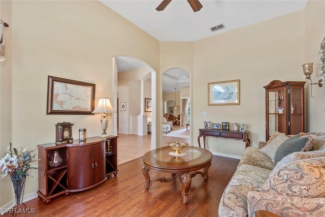 living area with arched walkways, visible vents, ceiling fan, wood finished floors, and baseboards