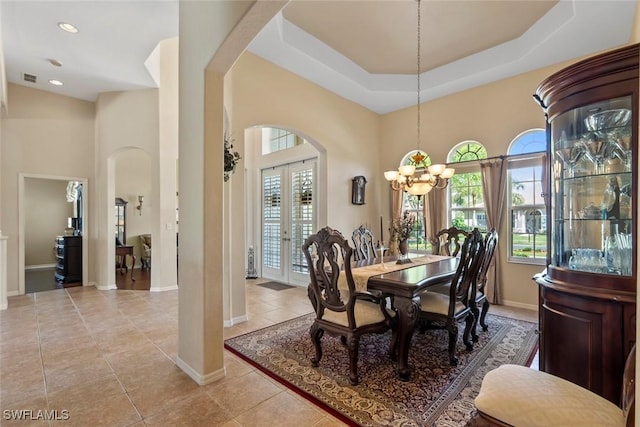 dining area with light tile patterned floors, arched walkways, a raised ceiling, and french doors