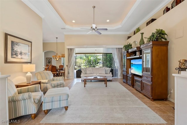 living room with light tile patterned floors, arched walkways, ceiling fan with notable chandelier, ornamental molding, and a tray ceiling