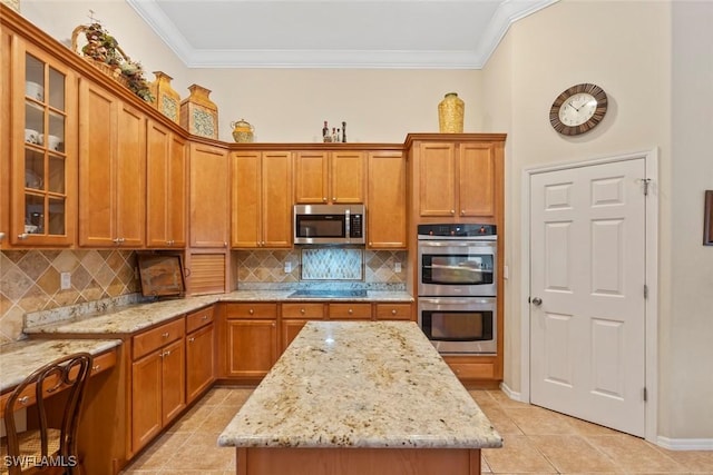 kitchen with light stone counters, a center island, crown molding, stainless steel appliances, and brown cabinetry