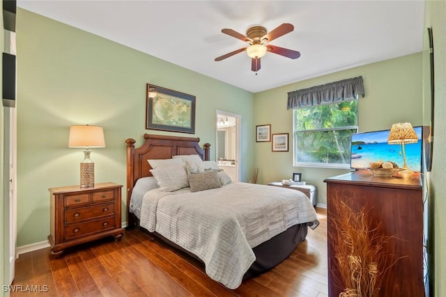 bedroom featuring ensuite bath, dark wood finished floors, a ceiling fan, and baseboards