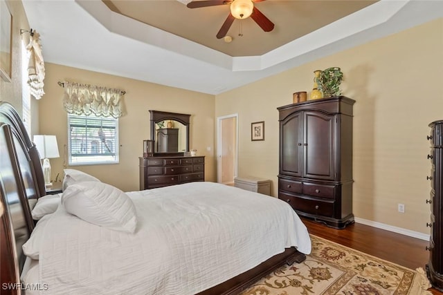 bedroom featuring ceiling fan, baseboards, a raised ceiling, and dark wood finished floors