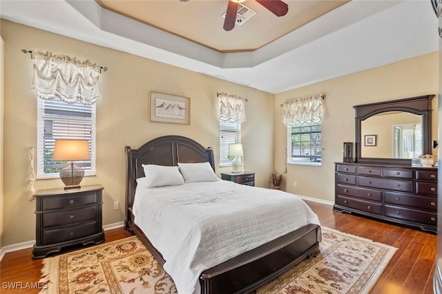 bedroom featuring wood finished floors, a raised ceiling, a ceiling fan, and baseboards