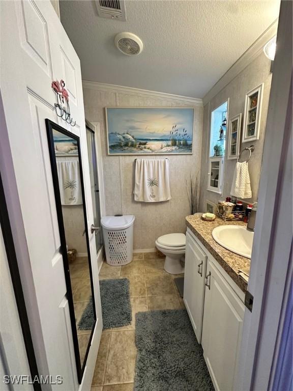 bathroom with a textured ceiling, visible vents, and ornamental molding