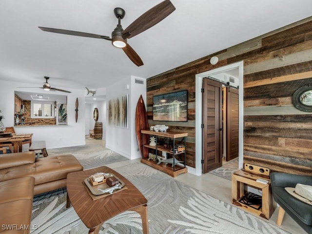 living area with ceiling fan, a barn door, and wooden walls