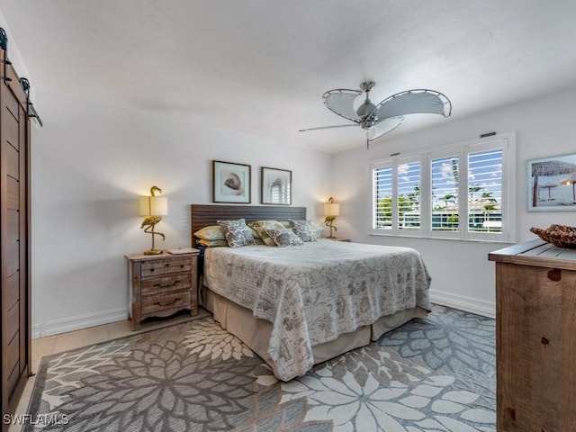 bedroom featuring light tile patterned floors, a barn door, a ceiling fan, and baseboards