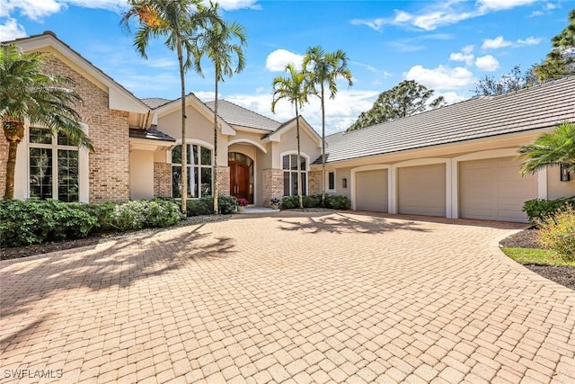 view of front of house with brick siding, driveway, an attached garage, and stucco siding