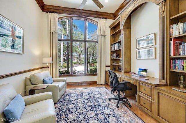 office area with light wood-style flooring, ornamental molding, ceiling fan, and built in desk