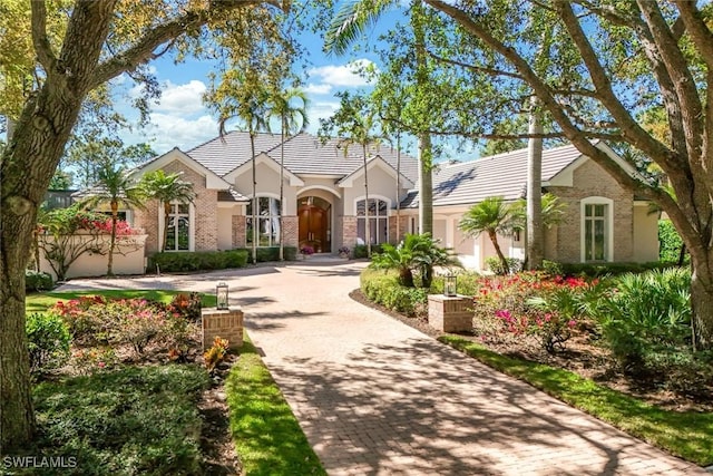 view of front facade featuring a garage, a tile roof, decorative driveway, and brick siding