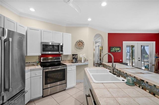 kitchen featuring tile counters, appliances with stainless steel finishes, a sink, and ornamental molding