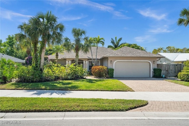 ranch-style house featuring decorative driveway, stucco siding, an attached garage, a front yard, and fence