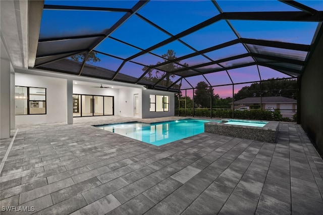 3233 64th St SW, Naples, FL 34105 - pool at dusk featuring a patio area, a pool with connected hot tub, a ceiling fan, and glass enclosure