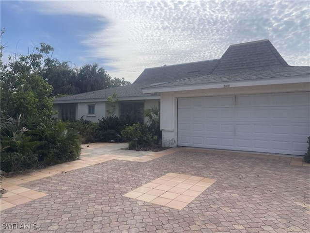 single story home with a garage, roof with shingles, decorative driveway, and stucco siding