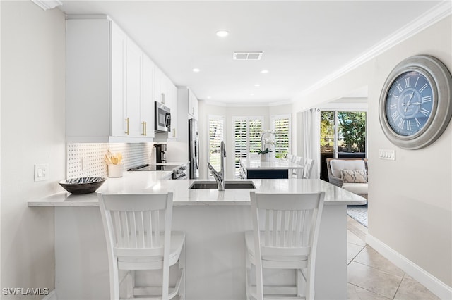 kitchen featuring light tile patterned flooring, a sink, appliances with stainless steel finishes, crown molding, and tasteful backsplash