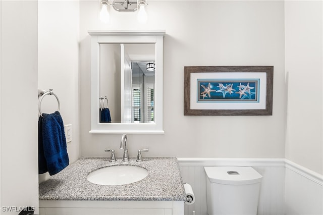 half bath with vanity, toilet, and a wainscoted wall