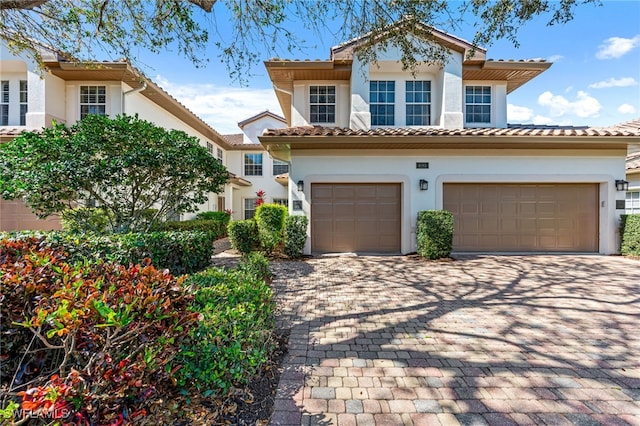 mediterranean / spanish-style home with decorative driveway, an attached garage, a tile roof, and stucco siding