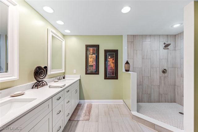 bathroom with a tile shower, double vanity, a sink, and baseboards