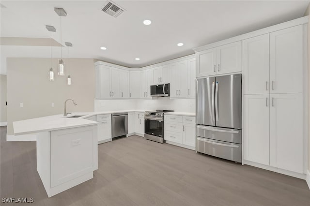 kitchen with a peninsula, a sink, visible vents, appliances with stainless steel finishes, and pendant lighting