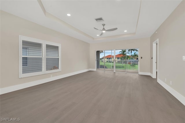 empty room with wood finished floors, a raised ceiling, visible vents, and baseboards