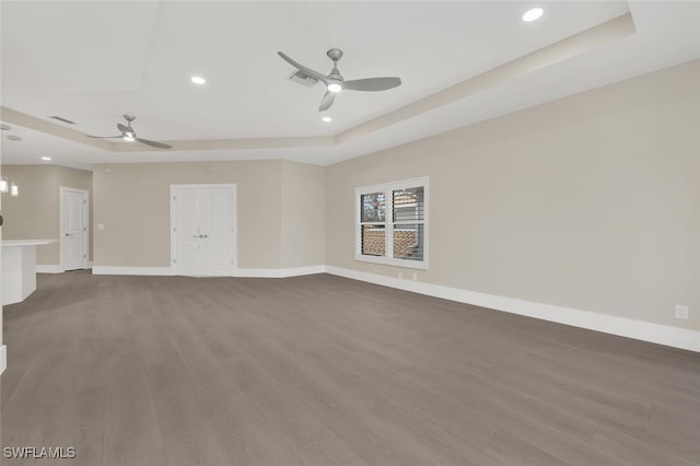 unfurnished living room with a tray ceiling, baseboards, visible vents, and dark wood-type flooring