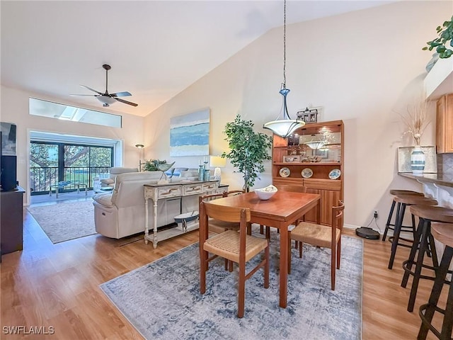 dining area with light wood-style floors, ceiling fan, high vaulted ceiling, and baseboards