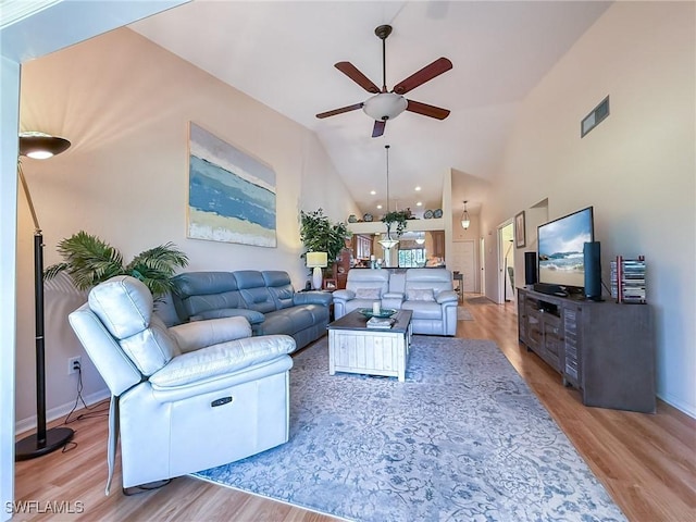 living area with light wood finished floors, visible vents, baseboards, ceiling fan, and high vaulted ceiling