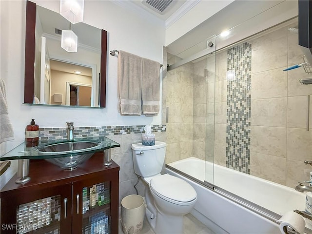 bathroom with tile walls, bath / shower combo with glass door, visible vents, toilet, and ornamental molding