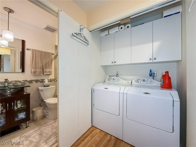 laundry room featuring a sink, visible vents, tile walls, independent washer and dryer, and cabinet space