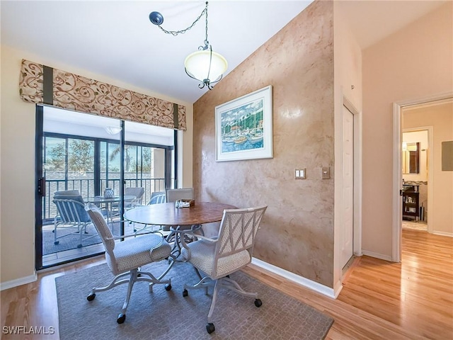 dining space with light wood-type flooring, vaulted ceiling, and baseboards