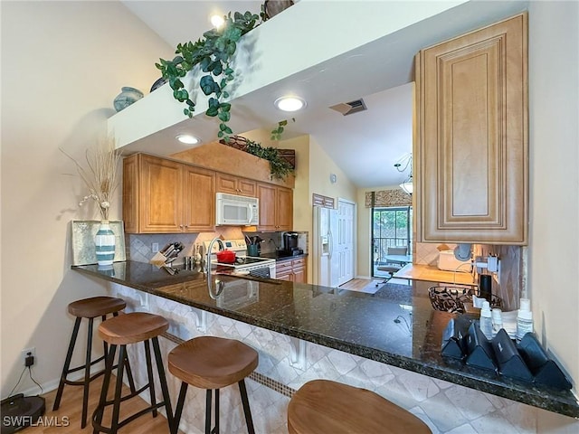 kitchen with lofted ceiling, visible vents, backsplash, white appliances, and a peninsula