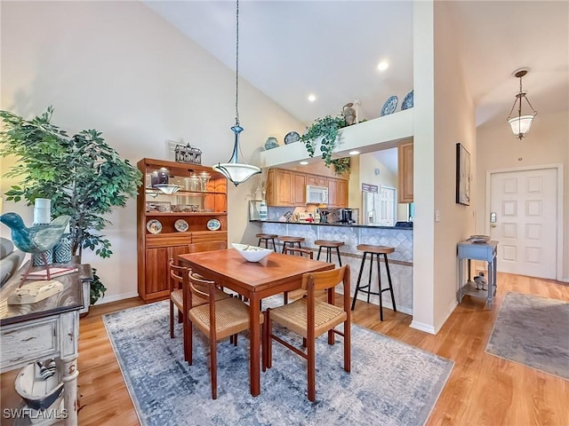 dining room with high vaulted ceiling, light wood finished floors, and baseboards