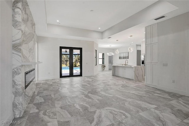 unfurnished living room featuring a high end fireplace, visible vents, french doors, a raised ceiling, and a sink