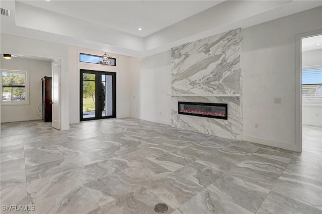 unfurnished living room with french doors, plenty of natural light, baseboards, and a premium fireplace