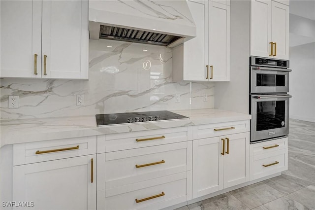 kitchen featuring light stone counters, premium range hood, stainless steel double oven, white cabinetry, and black electric stovetop