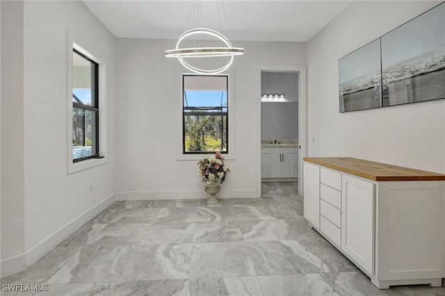 unfurnished dining area featuring an inviting chandelier, baseboards, and marble finish floor