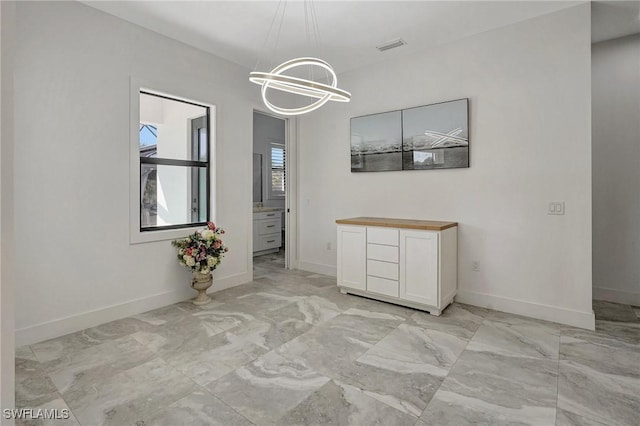 unfurnished dining area with visible vents, baseboards, marble finish floor, and an inviting chandelier